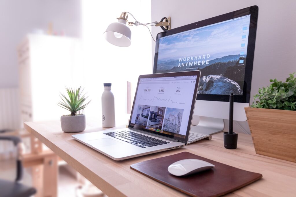 A laptop, big desktop, mouse, water bottle, bulb, planters at the table