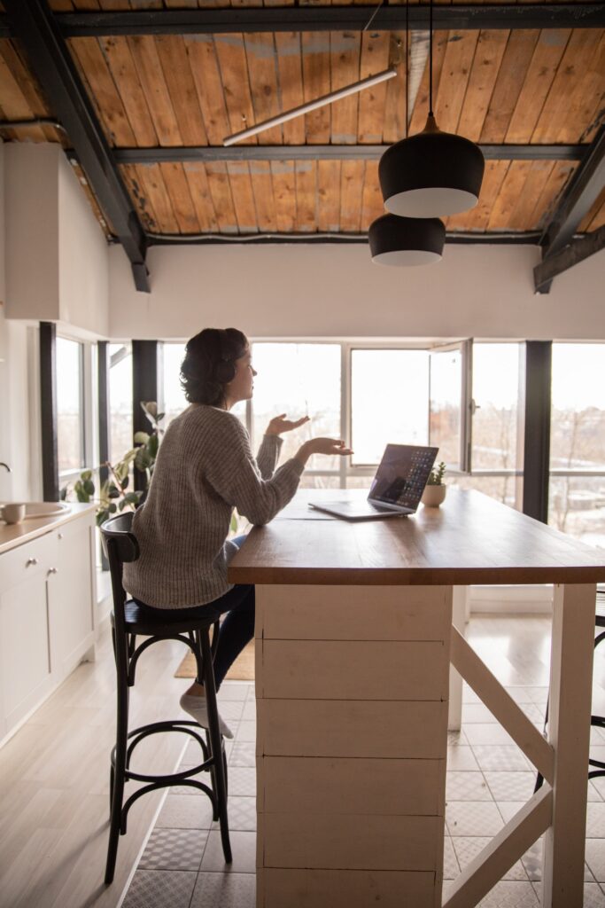 A lady talking to someone over the kitchen counter with a laptop on the table, working from home