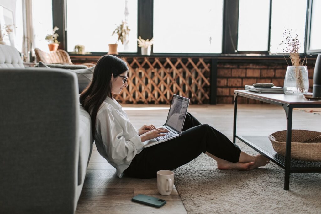 A lady sitting on the floor of her living room working on a laptop, she is an entrepreneur, working from home