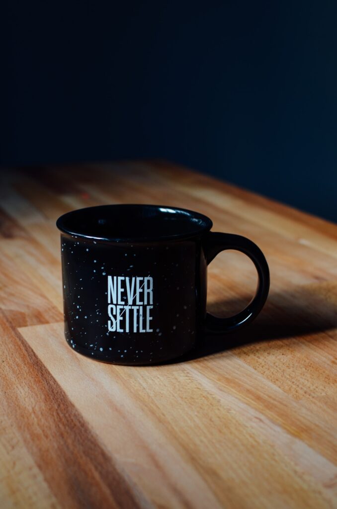 A coffee mug on a wooden table which says 'Never Settle'