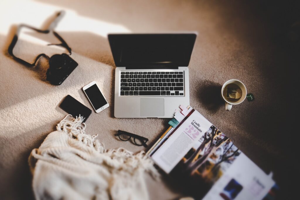 A laptop, a book, coffee mug, shawl, phones, camera on the carpeted floor